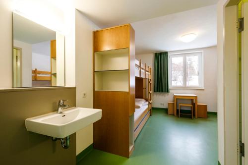 a bathroom with a sink and a bed and a mirror at Jugendherberge Bad Tölz in Bad Tölz