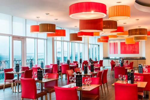 a restaurant with red chairs and tables and windows at Park Inn by Radisson Palace in Southend-on-Sea