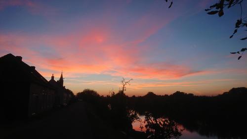 a sunset over a river with buildings and trees at B&B de Linge in Gellicum