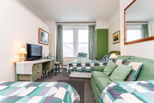 a room with two beds and a desk with a television at The Ravensbourne Hotel in Bournemouth