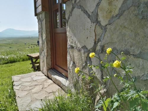 a stone building with a door and yellow flowers at Family Farm Bungalow in Žabljak