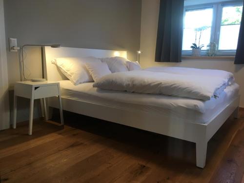 een groot bed met witte lakens en een nachtkastje bij Wohnung in zentraler Lage im Rheintal in Götzis