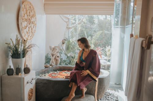 a woman sitting in a bathtub in a room at Kuwarasan A Pramana Experience in Ubud