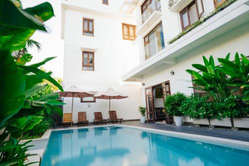 a swimming pool in front of a building with umbrellas at Hoi An Lotus Aroma Villa in Hoi An