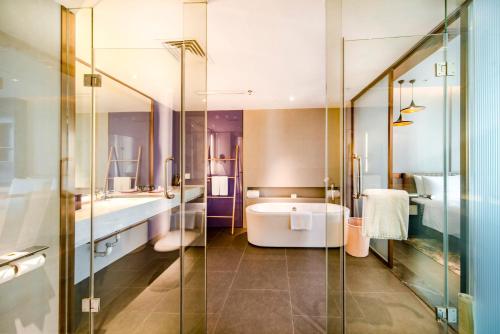 bagno con vasca e doccia in vetro di Q Hotel Haikou Meilan a Haikou