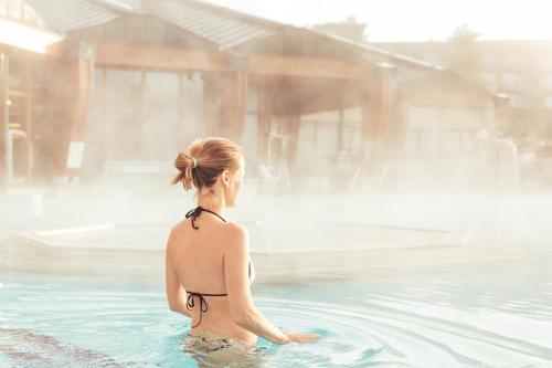 a woman sitting in the water in a swimming pool at Hotel Vier Jahreszeiten Loipersdorf in Loipersdorf bei Fürstenfeld