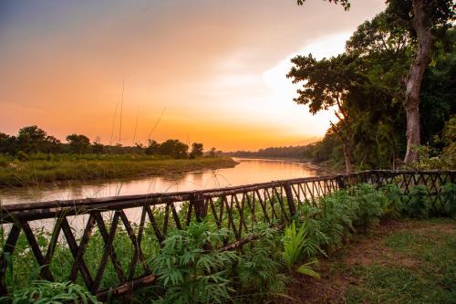 a bridge over a river at sunset at Chitwan Riverside Resort in Sauraha