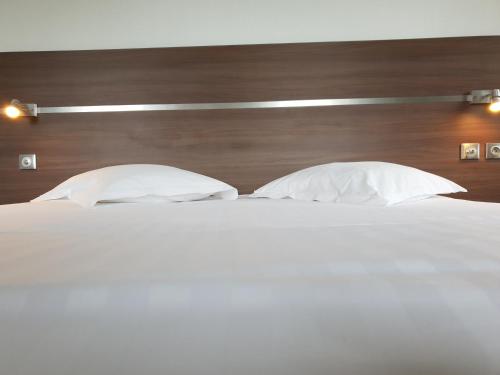a bed with two white pillows and a wooden headboard at Grand Hôtel Bénodet Abbatiale Riviera Bretonne in Bénodet