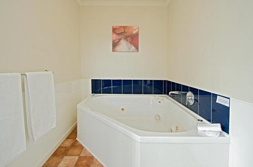 a white bath tub in a bathroom with blue tiles at Gateway Motor Inn in Mount Maunganui