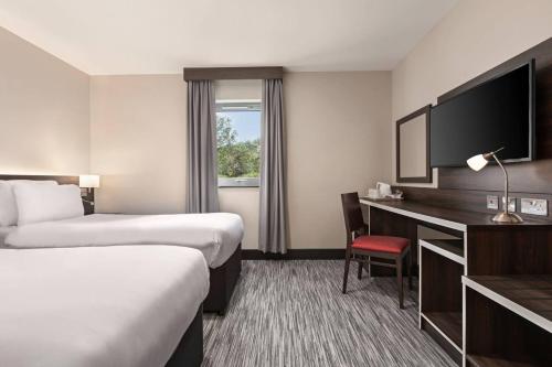 a hotel room with two beds and a desk and a television at Ramada by Wyndham Cobham in Cobham