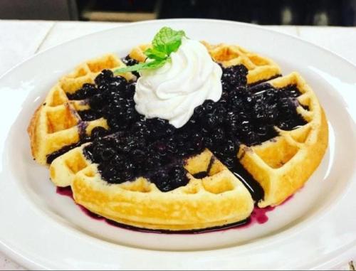弗林弗隆Victoria Inn Flin Flon的盘子里放着一块华夫饼，淋上黑莓酱和鲜奶油。