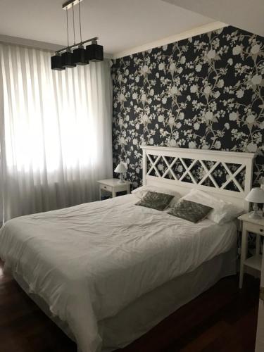 um quarto com uma cama branca e papel de parede floral em albobide em Bakio