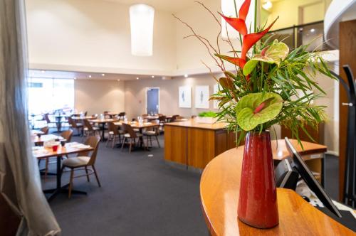 a red vase with flowers on a table in a restaurant at West Plaza Hotel in Wellington