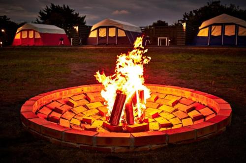 a fire pit in a field with tents in the background at Chikura Tsunagu Hotel in Minamiboso