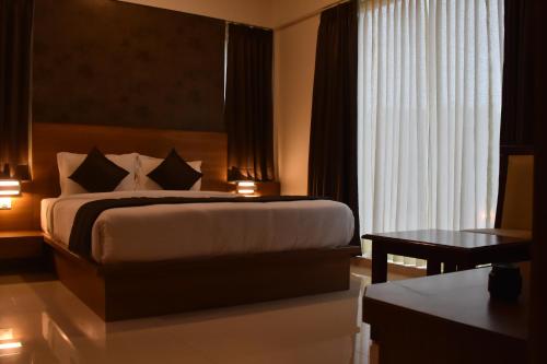 ein Hotelzimmer mit einem Bett, einem Tisch und einem Fenster in der Unterkunft Heritage Inn in Mysore