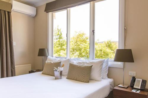 a bedroom with a white bed with a large window at Peppers Craigieburn Resort in Bowral