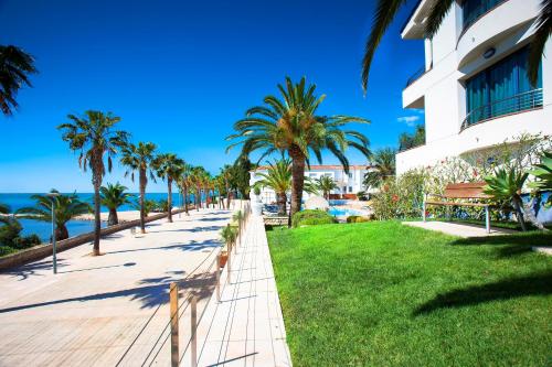 a walkway near the beach with palm trees and a building at Miami Mar - Boutique Hotel & Restaurante in Sant Carles de la Ràpita