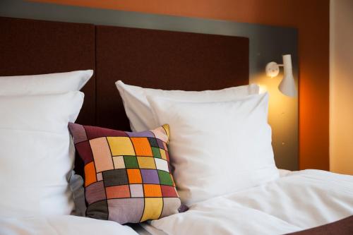 a bed with white sheets and pillows with a colorful pillow at Hotel Koldingfjord in Kolding