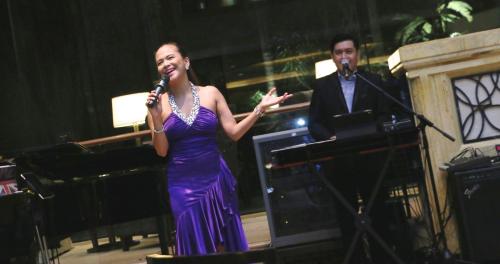 a woman in a purple dress singing at a piano at Shangri-La Kuala Lumpur in Kuala Lumpur