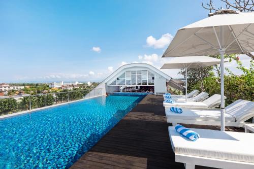 a swimming pool with two lounge chairs and an umbrella at Jambuluwuk Oceano Seminyak Hotel in Seminyak