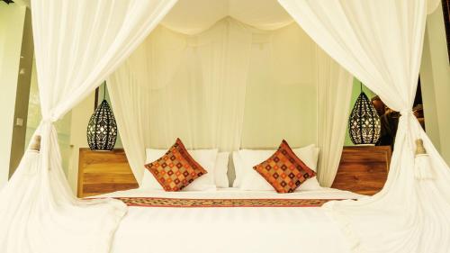 a bedroom with a white bed with white curtains and pillows at Cahaya Indah Villas in Ubud