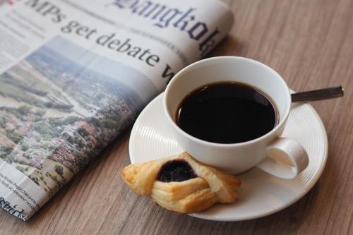 a cup of coffee and a pastry on a plate next to a newspaper at Eleven Hotel Bangkok Sukhumvit 11 in Bangkok