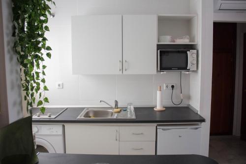 eine Küche mit weißen Schränken, einer Spüle und einer Mikrowelle in der Unterkunft centrico apartamento nuevo, zona corte ingles in Málaga