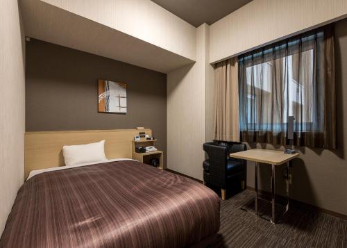 旭川市にあるホテルルートインGrand旭川駅前のベッド、デスク、窓が備わるホテルルームです。