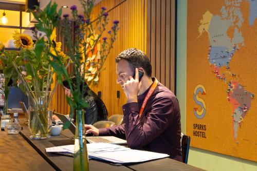 a man sitting at a table talking on a cell phone at Sparks Hostel in Rotterdam