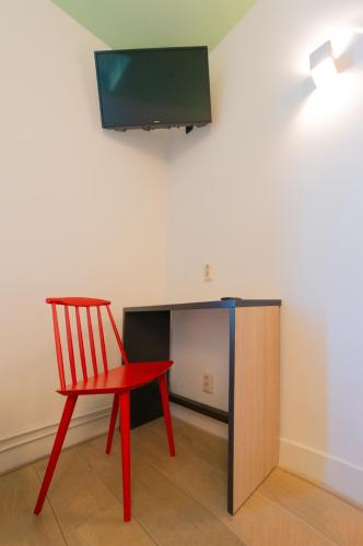 a red chair and a desk with a television on a wall at Sparks Hostel in Rotterdam