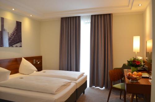 ein Hotelzimmer mit 2 Betten, einem Schreibtisch und einem Tisch in der Unterkunft Augusten Hotel München in München