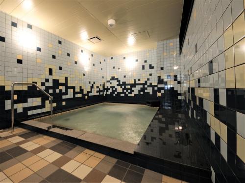 una gran piscina en un baño con azulejos blancos y negros en Green Rich Hotel Tottori Ekimae (Artificial hot spring Futamata Yunohana) en Tottori