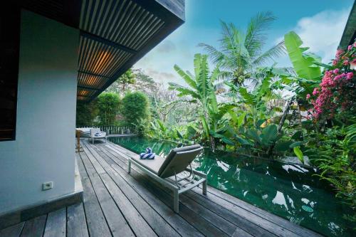 een huis met een zwembad en een stoel op een houten terras bij Surya Kembar Villas in Ubud