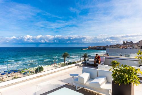 a woman sitting on a balcony overlooking the ocean at Victoria Palace Cefalù in Cefalù