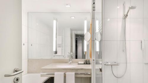 a bathroom with a sink and a shower with a mirror at Dorint Hotel am Heumarkt Köln in Cologne