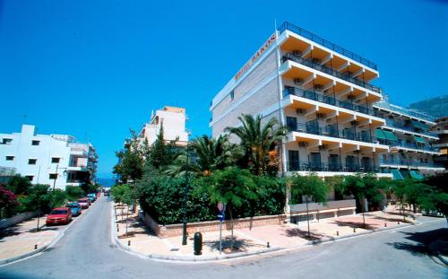 a building on a city street with palm trees and cars at Hotel Bakos in Loutraki