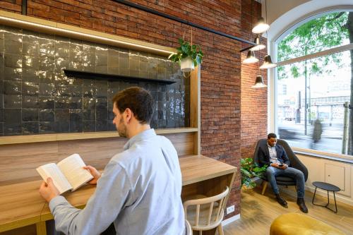 a man reading a book in a restaurant with another man sitting at B&B HOTEL Brussels Centre Gare du Midi in Brussels