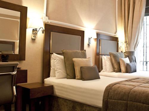 a hotel room with two beds and a mirror at Gem Strathmore Hotel in London