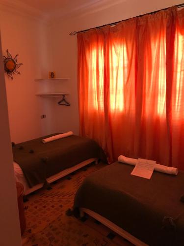 two beds in a room with red curtains at Hôtel Riad Gnaoua in Essaouira