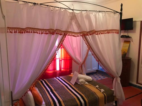 a bedroom with a canopy bed with curtains at Hôtel Riad Gnaoua in Essaouira