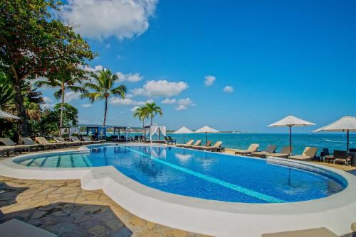 una piscina vicino all'oceano con sedie e ombrelloni di Velero Beach Resort a Cabarete