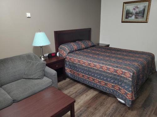 ein Schlafzimmer mit einem Bett, einem Sofa und einem Stuhl in der Unterkunft Battlefords Inn in North Battleford