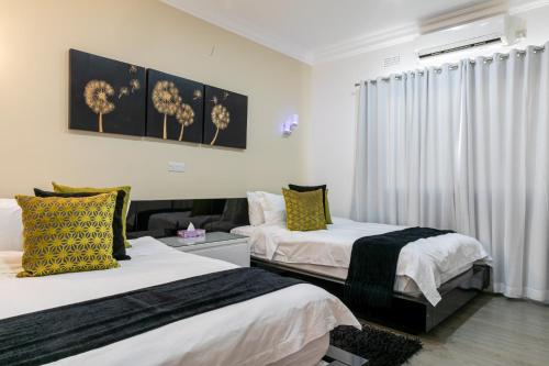 two beds in a room with white walls and yellow pillows at Fallsway Villas in Lusaka