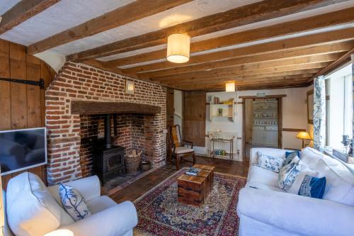 a living room with white furniture and a brick fireplace at Primrose Cottage at The Shippe in Bridge