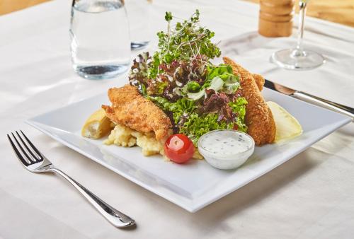 a white plate with fish and salad on a table at Hotel Die Pflegerbrücke in Salzburg