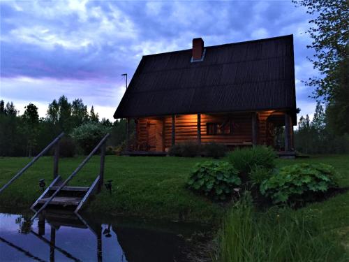 une cabane en rondins avec un étang en face de celle-ci dans l'établissement Pirts Baudas, à Sīveci