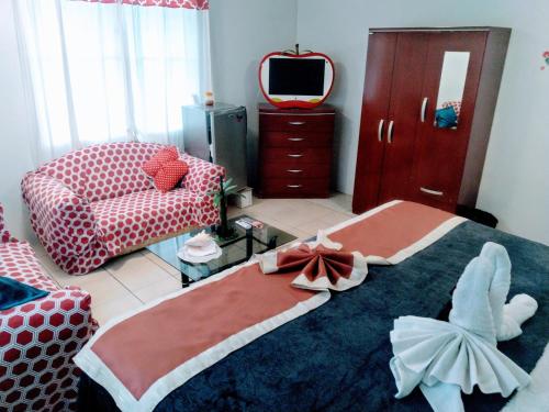 a bedroom with a bed and a couch and a tv at The Red Hut Inn in Belize City