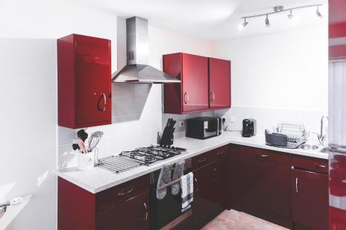 a kitchen with red cabinets and a stove at Salford Holiday Apartment Manchester in Manchester