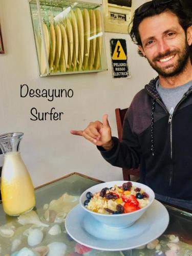 a man pointing at a bowl of cereal and a bowl of orange juice at Surf hostel My Friends in Huanchaco