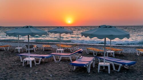 a group of chairs and umbrellas on the beach at sunset at Sirene Beach Hotel in Ixia